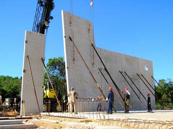 Construction workers securing tall vertical slabs of concrete, tilting them from horizontal to vertical.